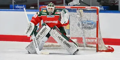 Man sieht einen Eishockeyspieler in Eishockeymontur im Tor stehen in einem Stadion.