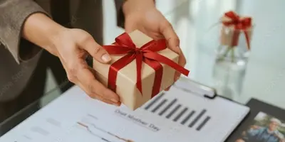 Auf dem Bild sind Hände zu sehen, die ein Geschenk über einem Bürotisch halten.