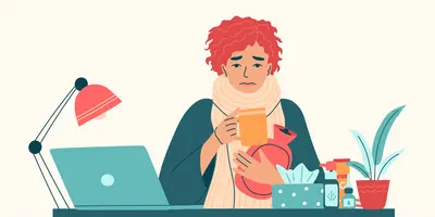 Person, die im Schal und einer Tasse und Wärmeflasche in den Händen und sich offensichtlich krank fühlt, vor ihrem Schreibtisch mit Laptop sitzt.