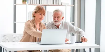 Das Bild zeigt zwei ältere Menschen vor einem laptop. Es steht symbolisch für "Unretirement", den Wiedereinstieg von Rentner:innen ins Arbeitsleben.