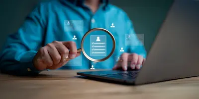 Zu sehen ist der Oberkörper eines Menschen, der vor einem Laptop sitzt. In der Hand hält er eine Lupe und ist umgeben von Graphiken, die symbolisch für Background-Checks von Bewerbenden stehen.