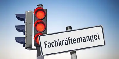 Das Bild zeigt ein Schild mit der Aufschrift "Fachkräftemangel". Die rote Ampel daneben symbolisiert den Ernst der Lage.