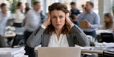 Das Bild zeigt eine Frau in einem Büro, die sich genervt die Ohren zuhält. Im Hintergrund sind verschwommen Menschen und Geräte zu sehen, die für den Lärm verantwortlich sind.