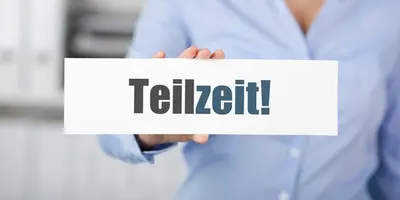 Zu sehen ist eine Frau in Büroumgebung, die ein Stück Papier mit der Aufschrift "Teilzeit" in der Hand hält.